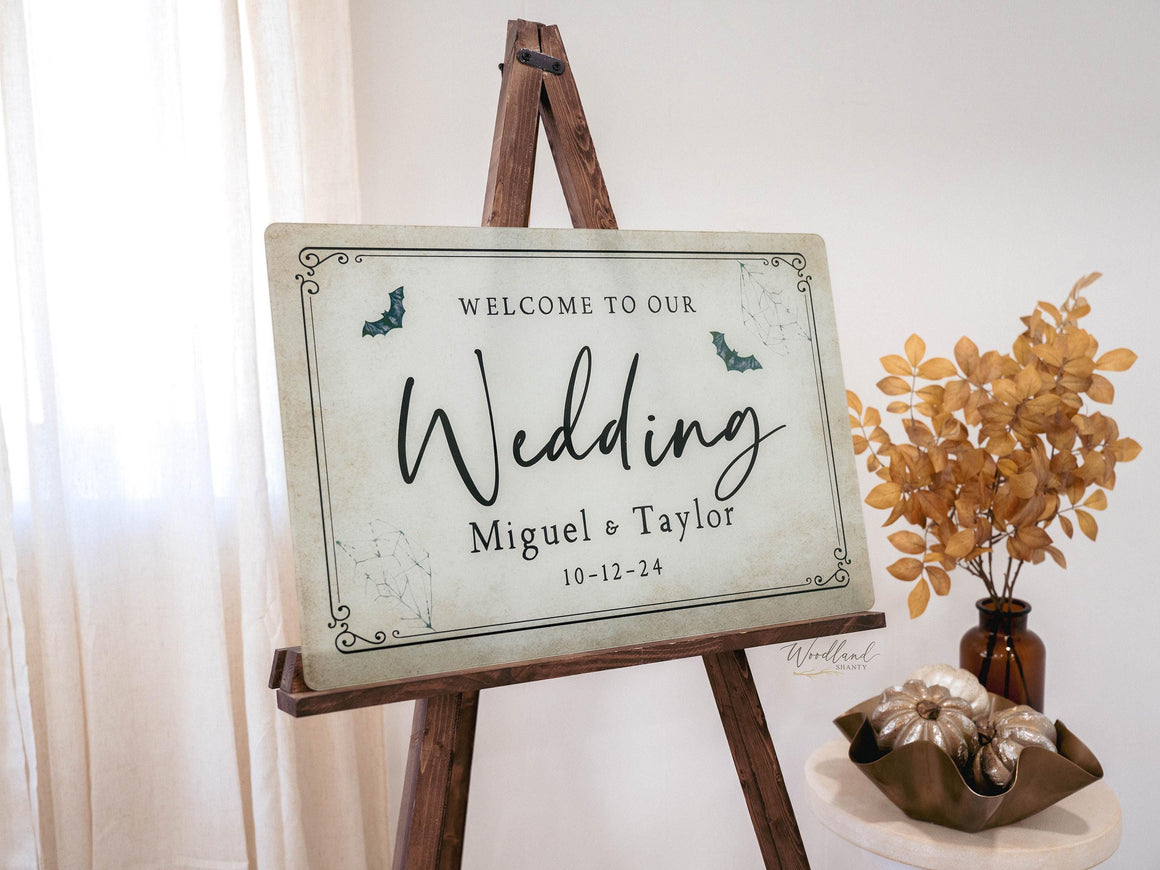 May include: A vintage-style wedding sign with a rustic wooden easel. The sign is decorated with bats and reads "Welcome to our Wedding Miguel & Taylor 10-12-24".