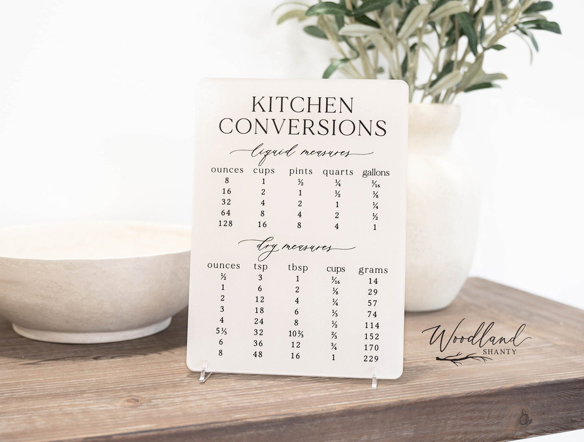 Kitchen conversions sign is 9 inches tall, 6.5 wide made of acrylic and comes with 2 acrylic feet to stand it up on. It features liquid and dry measurements and shows conversions for ounces, cups, pints, quarts, gallons, tsp, tbsp, cups and grams.